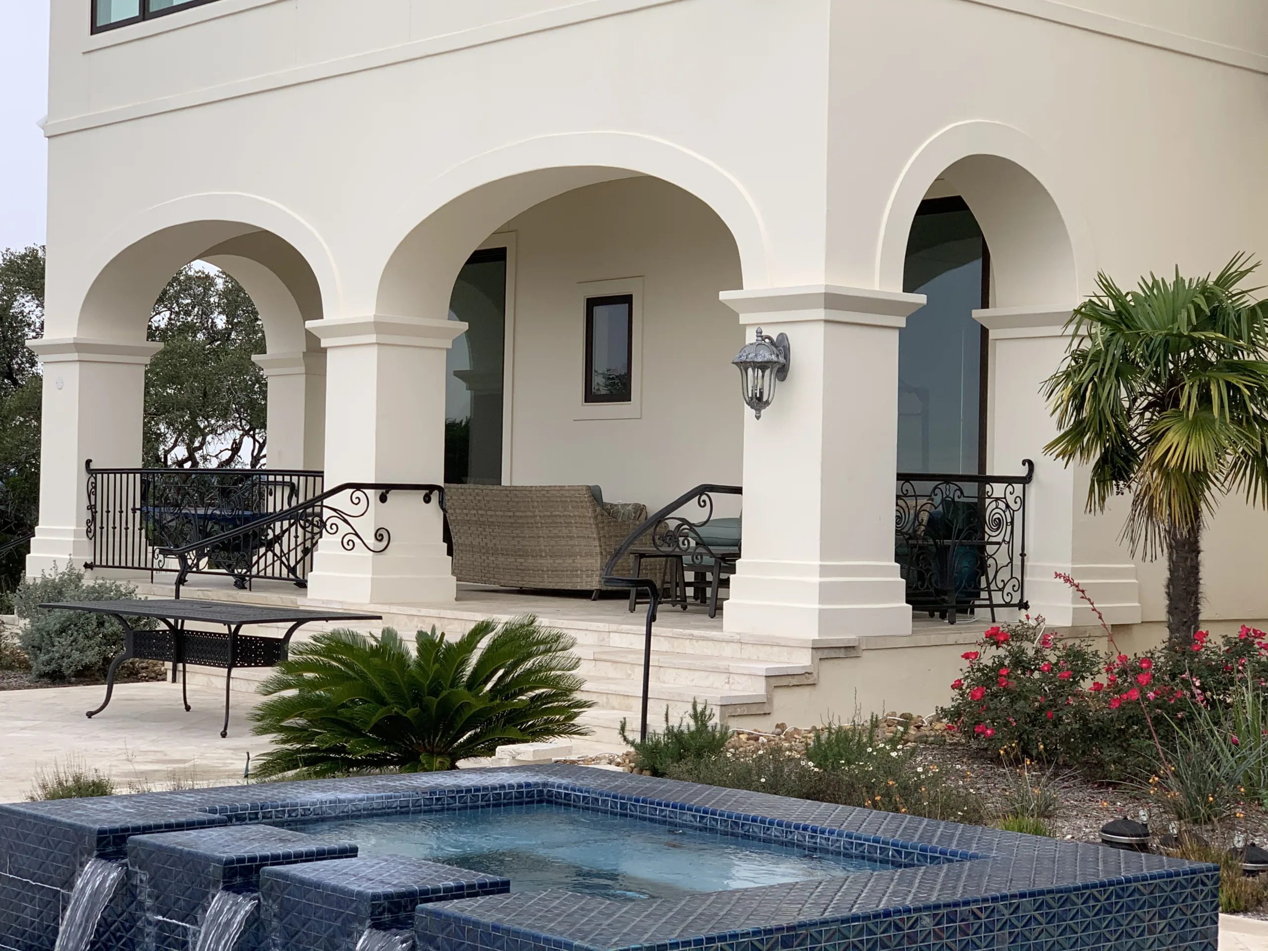 Luxury residential patio featuring white stucco arches, decorative wrought iron railings, custom stair handrails, and elegant architectural details.